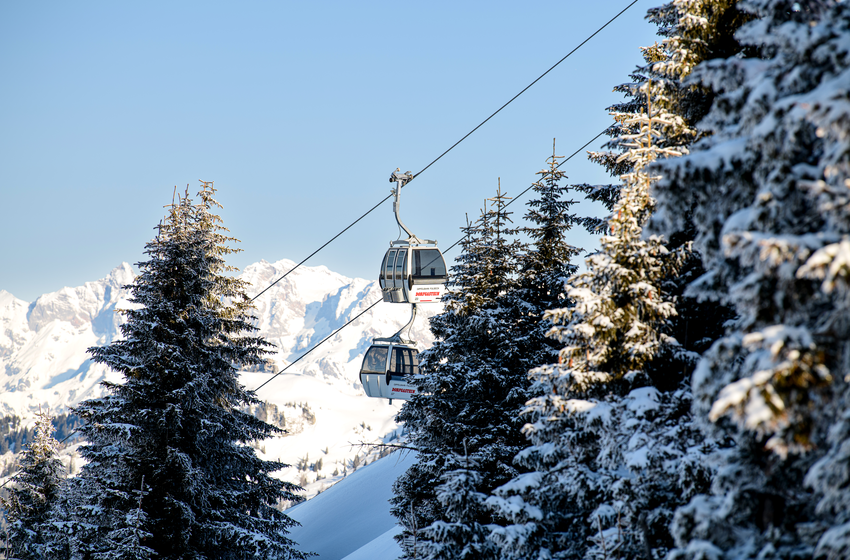 Zwei Gondeln einer Seilbahn fahren zwischen schneebedeckten Bäumen vor Bergkulisse bei klarem Winterhimmel | © Dorfgasteiner Bergbahnen AG