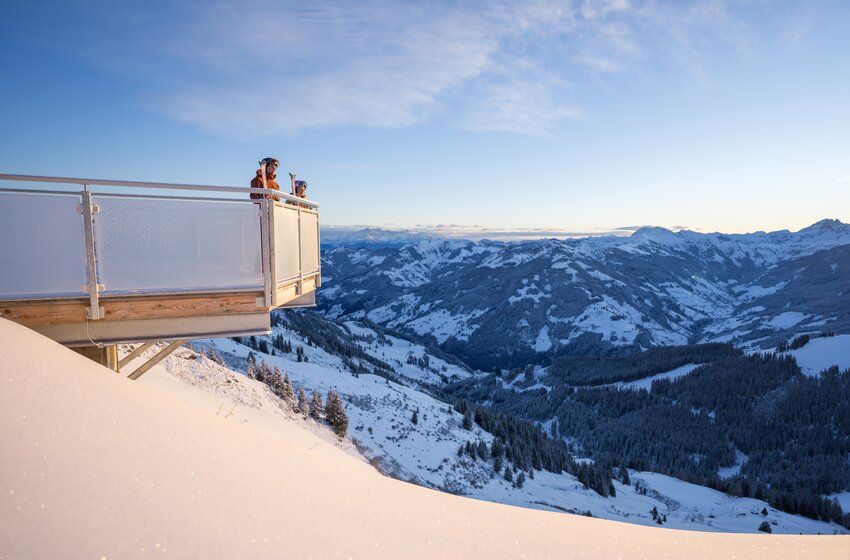 Two people stand on a viewing platform overlooking a snow-covered valley with mountains and forested slopes | © Dorfgasteiner Bergbahnen AG