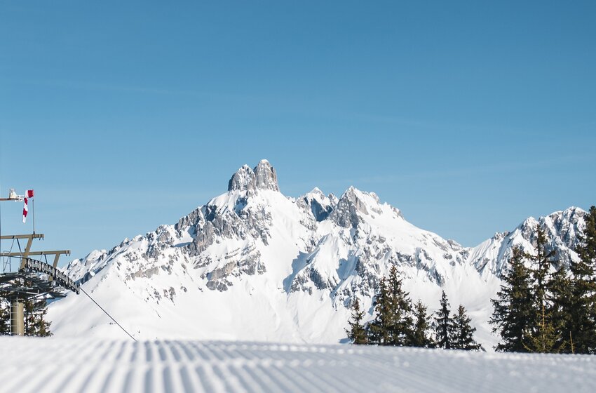 Freshly groomed ski slope with view of snow-covered peaks | © Bergbahnen Filzmoos GmbH View of groomed slope, snowy mountain peaks, ski lift station and fir trees in the foreground | © Bergbahnen Filzmoos GmbH