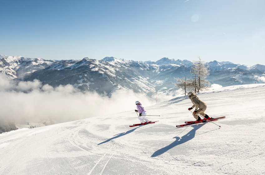 Two female skiers skiing side by side on sunny slope with Alpine mountain view | © Großarler Bergbahnen GmbH & Co KG