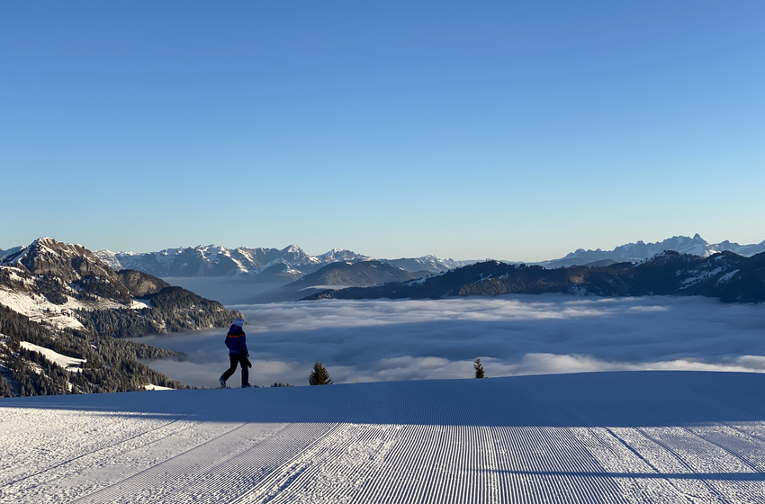 Person stands on freshly groomed ski slope overlooking foggy valley and peaks | © Großarler Bergbahnen GmbH & Co KG