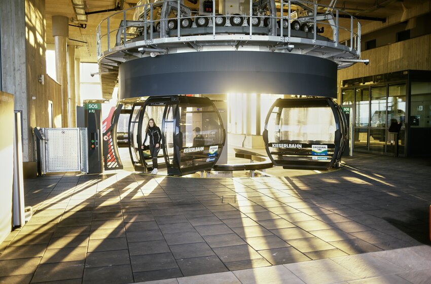 Gondelstation der Kieserlbahn mit Sonnenlicht und Fahrgast beim Einstieg, moderne Architektur und klare Lichtstrahlen. | © Grossarler Bergbahnen GmbH & Co KG