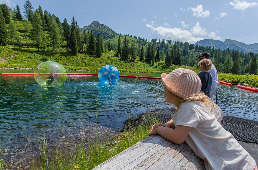 Children walk in water balls across a mountain lake while family watches in a sunny Alpine landscape | © Hauser Kaibling Seilbahn- und Liftges.m.b.H. & Co KG