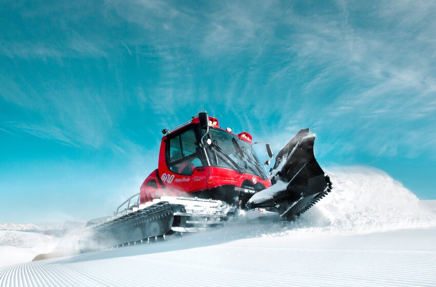 Red snow groomer with blade smooths snowy ski slope under clear sky in the Alpine mountains | © Hochkönig Bergbahnen GmbH