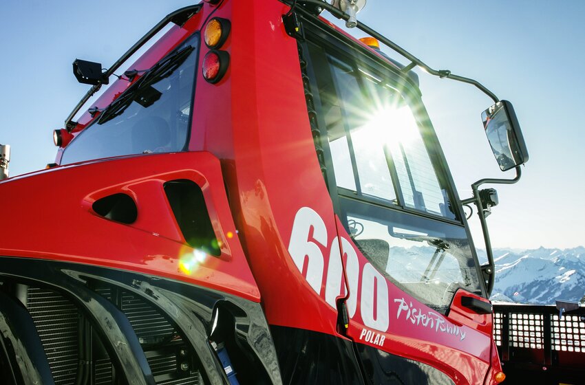 Close-up of red PistenBully 600 Polar with sunlight and Alpine mountain backdrop | © Hochkönig Bergbahnen GmbH
