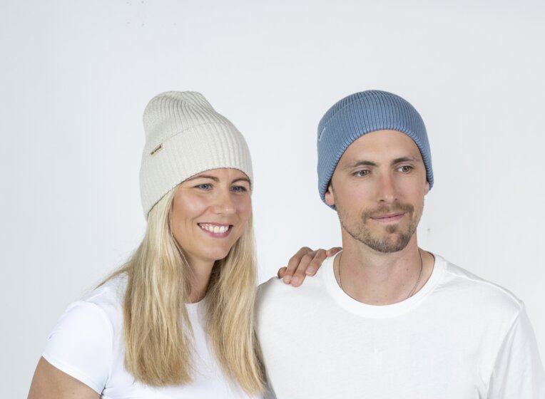 Mann und Frau mit Ski amadé Mützen posieren seitlich, Studio mit hellem Hintergrund | © Ski amadé GmbH / Lorenz Masser