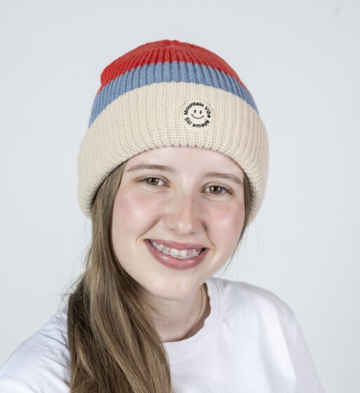 Smiling girl wearing red-beige Mountain Vibe Ski amadé beanie and white shirt | © Ski amadé GmbH / Lorenz Masser