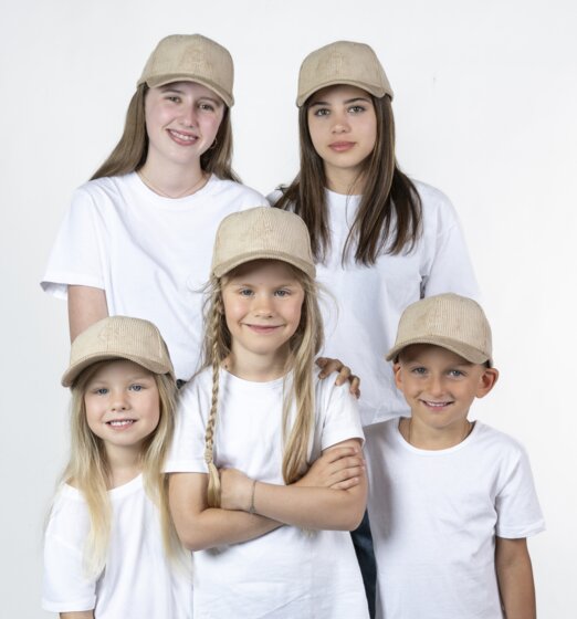 Five children wearing beige baseball caps and white T-shirts standing together in front of a light studio background | © Ski amadé GmbH / Lorenz Masser