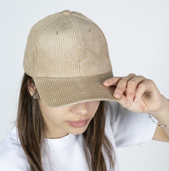 Girl wearing a beige cord baseball cap and white T-shirt holding the cap brim in front of a light studio background | © Ski amadé GmbH / Lorenz Masser