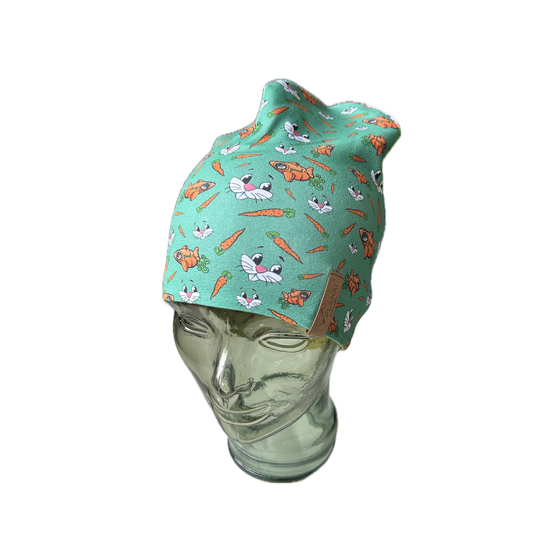 Green kids’ beanie on glass model head, printed with bunny faces, carrots and orange rabbits, leather tag on side | © Planai-Hochwurzen-Bahnen GmbH
