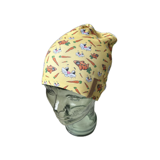 Yellow kids’ beanie on glass model head, printed with bunny faces, carrots and orange rabbits, leather tag on side | © Planai-Hochwurzen-Bahnen GmbH