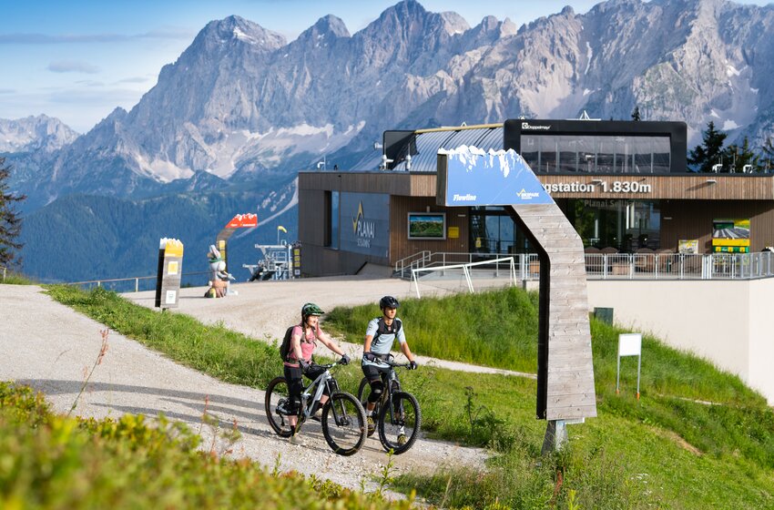 Two mountain bikers at Flowline start near Planai top station at 1830 m, with Dachstein range rising in the background | © Josh Absenger