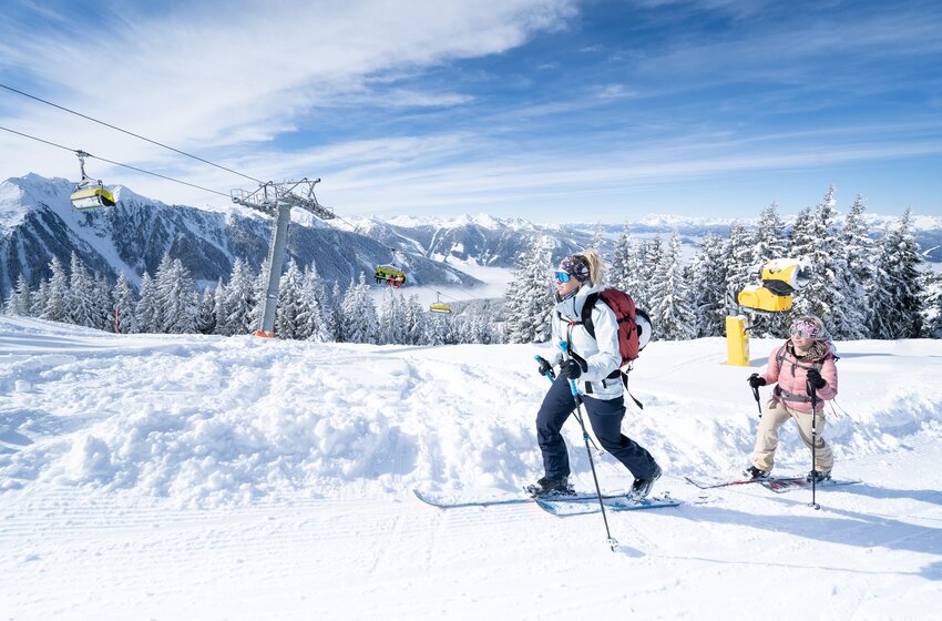 Zwei Skitourengeherinnen auf verschneiter Planai unterwegs Zwei Skitourengeherinnen steigen bei Sonnenschein über eine verschneite Planai-Piste mit Blick auf die Berge.