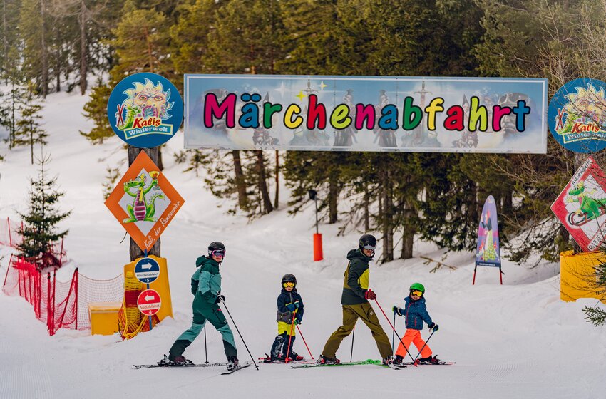 Eine Familie auf Skiern fährt durch das bunte Tor zur Märchenabfahrt „Kalis Winterwelt“ am verschneiten Rittisberg. | © Rittis-Lift Engelhardt GmbH & Co KG