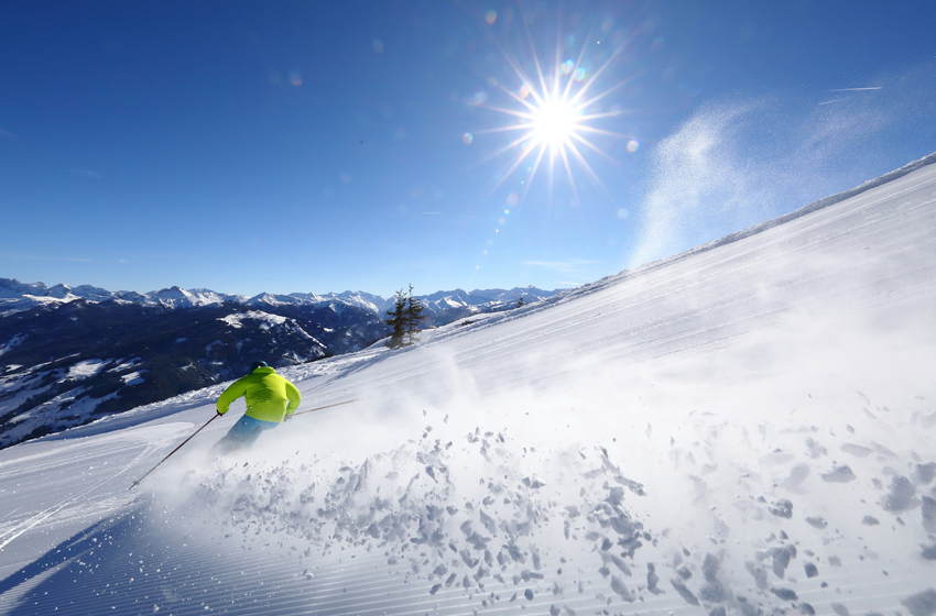 Skifahrer in greller Jacke fährt bei Sonnenschein durch frischen Pulverschnee mit weitem Alpenblick. | © Tourismusverband Großarltal