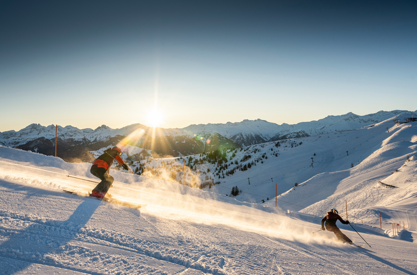 Zwei Wintersportler fahren bei Sonnenaufgang über frisch präparierte Piste im Großarltal mit Bergblick. | © Tourismusverband Großarltal