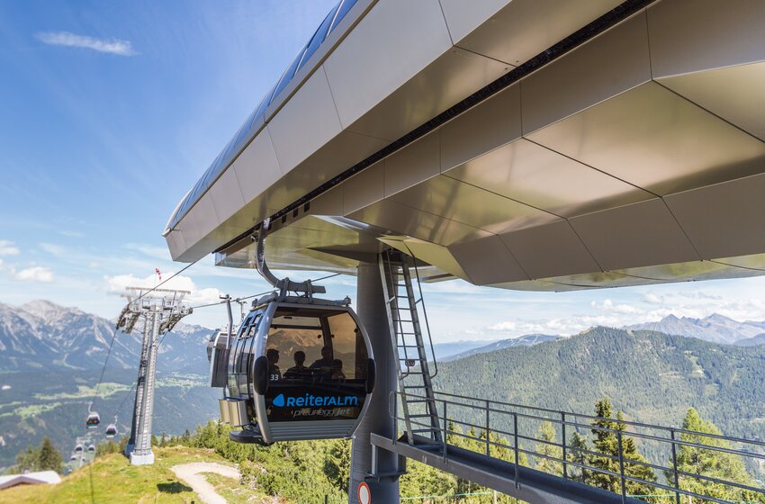 Modern gondola lift system at Reiteralm in summer | © Reiteralm Bergbahnen GmbH & Co.KG Preunegg Jet gondola at Reiteralm departs modern station, floating above green slopes with alpine panorama. | © Reiteralm Bergbahnen GmbH & Co.KG