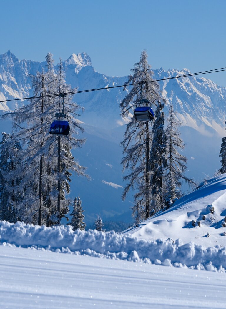 Zwei blaue Gondeln fahren an Seilbahn über verschneite Hügel mit vereisten Bäumen und Alpen im Hintergrund | © Ski amadé GmbH
