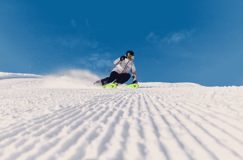 Skifahrer in weißer Jacke zieht einen Schwung auf präparierter Piste und wirbelt Schnee unter blauem Himmel auf | © Gasteiner Bergbahnen AG 