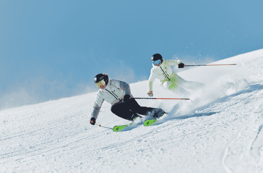 Zwei Skifahrer ziehen enge Schwünge auf einer verschneiten Piste und wirbeln dabei Schnee unter blauem Himmel auf. | © Gasteiner Bergbahnen AG 