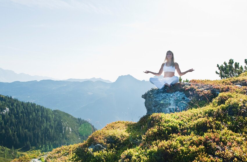 Woman meditating in white clothes in lotus pose on sunny rock with mountain panorama in background | © Zauchensee Liftgesellschaft Benedikt Scheffer GmbH