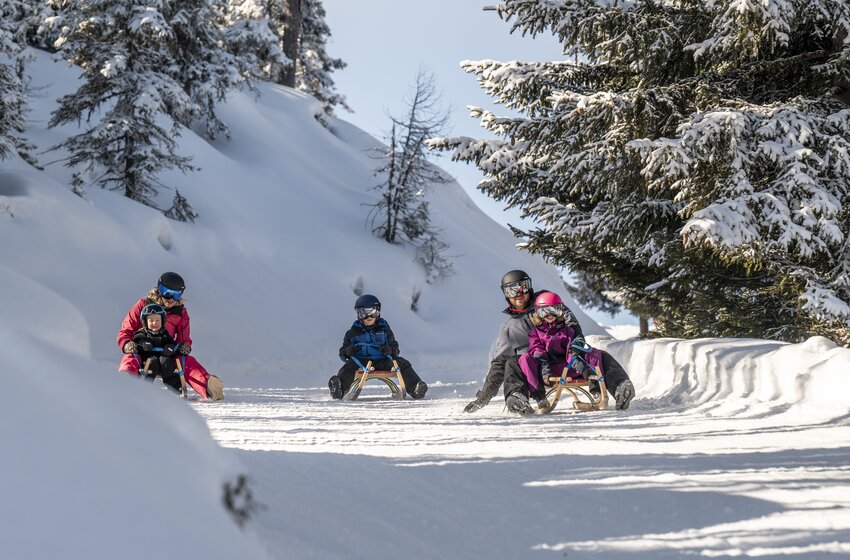 Vier Personen rodeln auf verschneiter Bahn durch winterlichen Nadelwald bei Sonne und blauem Himmel | © Zauchensee Liftgesellschaft Benedikt Scheffer GmbH